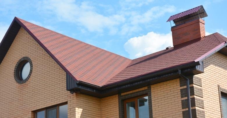 Close-up of a residential roof with red shingles and a brick chimney in The Woodlands Texas.