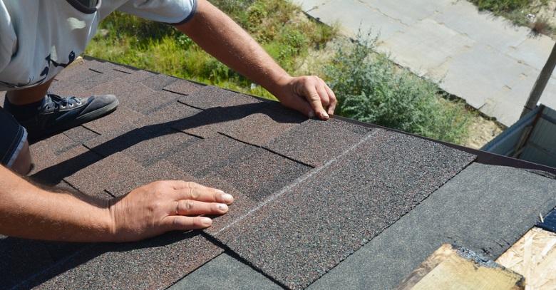 Close-up of a roofer's hands installing asphalt shingles on a roof.