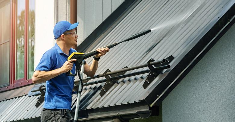 Roofing technician cleaning metal roof panels with a power washer in The Woodlands, Texas.