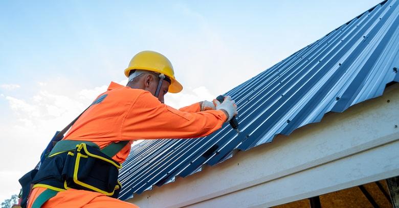 Worker in orange safety gear installing metal roofing on a house.
